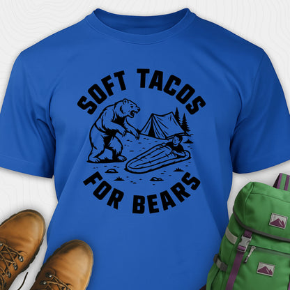 Blue funny bear shirt with bear graphic and text 'Soft Tacos for Bears' on a white background. surrounded by hiking boots and a green backpack.