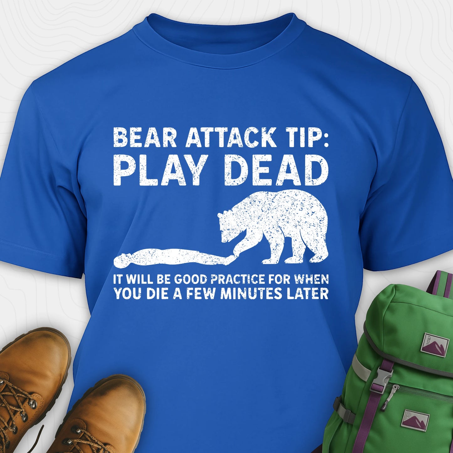Blue bear tee shirt with bear graphic and text, paired with hiking boots and a green backpack on a white background.