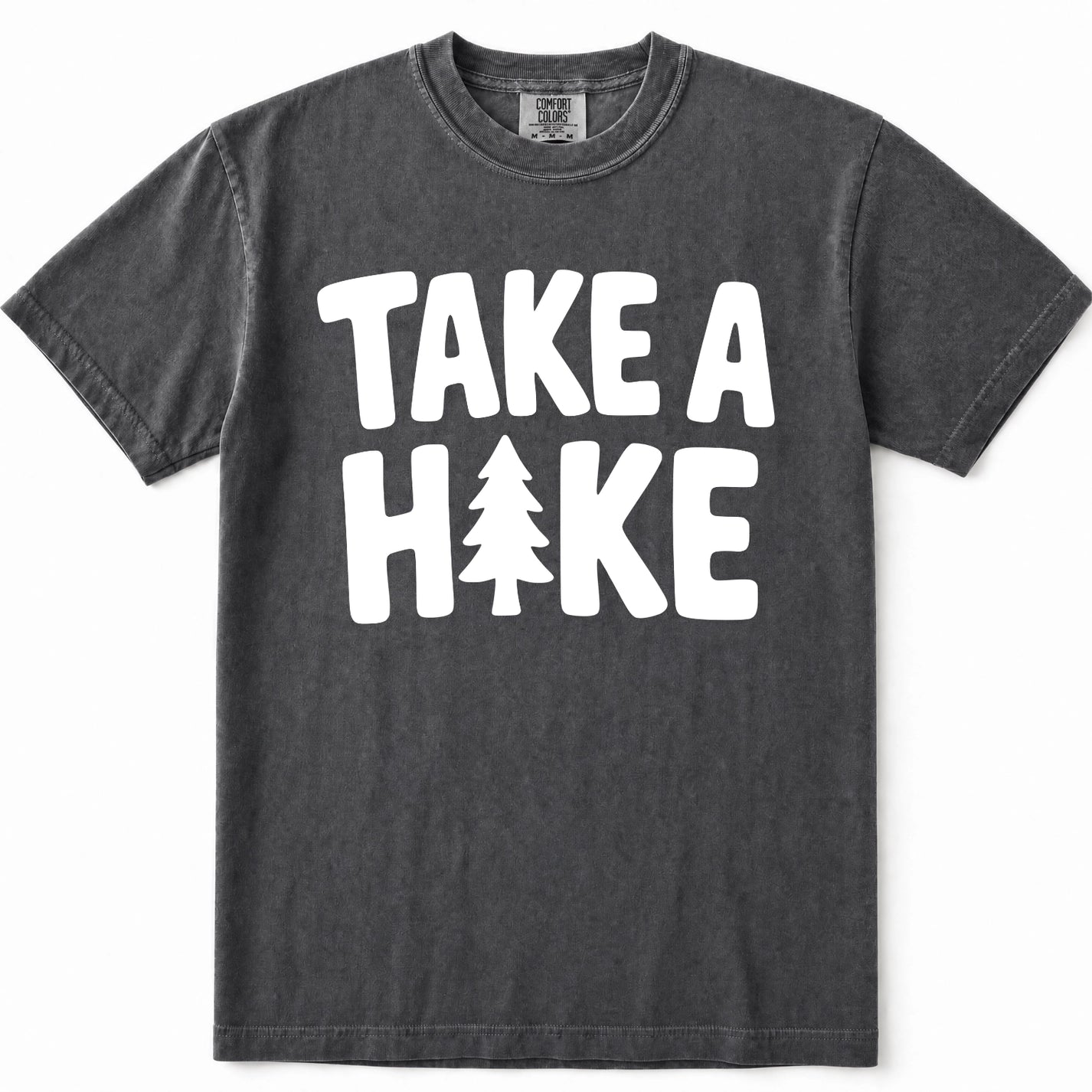 Pepper mineral-wash t-shirt with a bold white graphic print reading 'TAKE A HIKE' where the letter 'I' is replaced by a pine tree silhouette. The shirt is displayed flat against a clean white background.