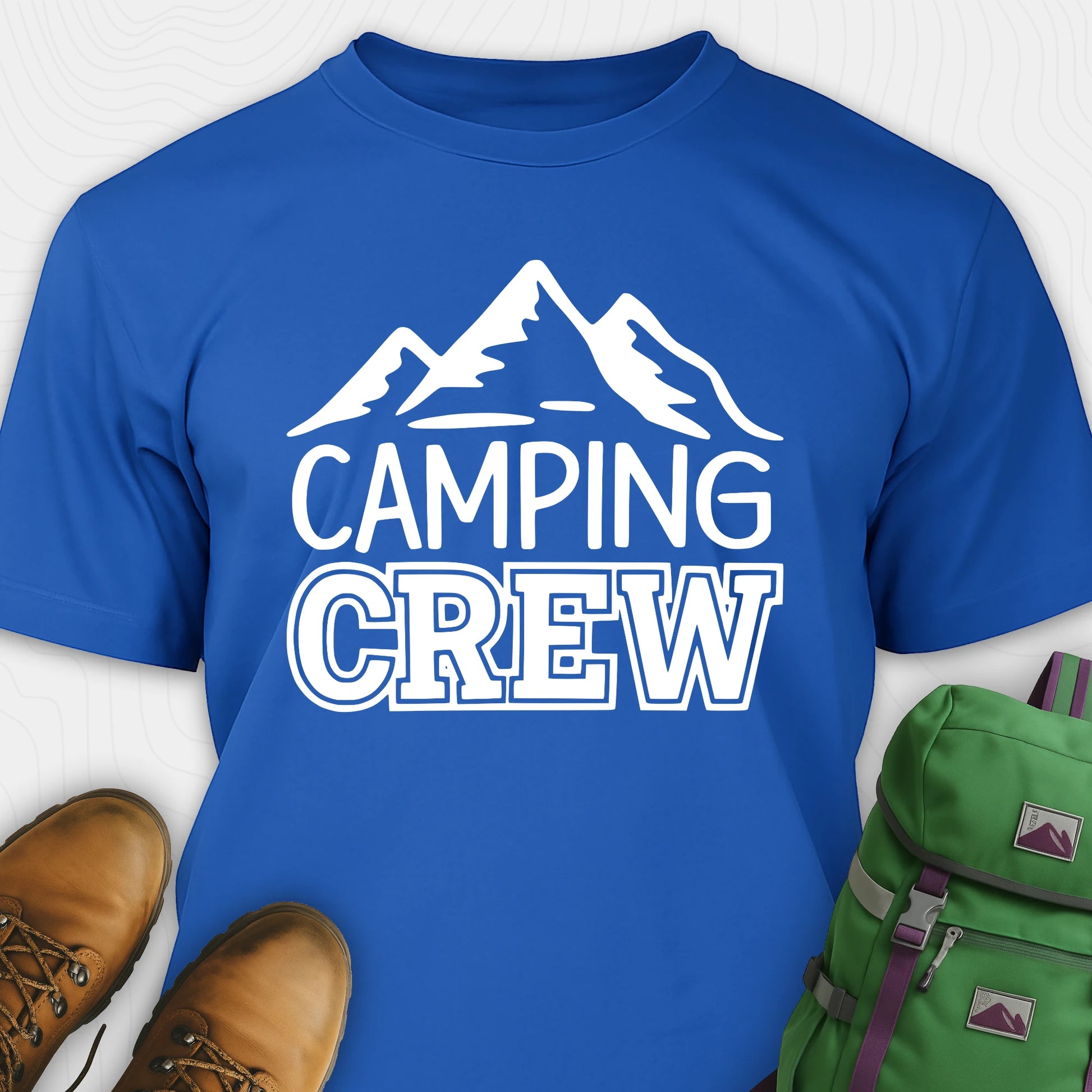 Blue camping crew t-shirt with 'Camping Crew' text and mountain graphic, paired with hiking boots and a green backpack.