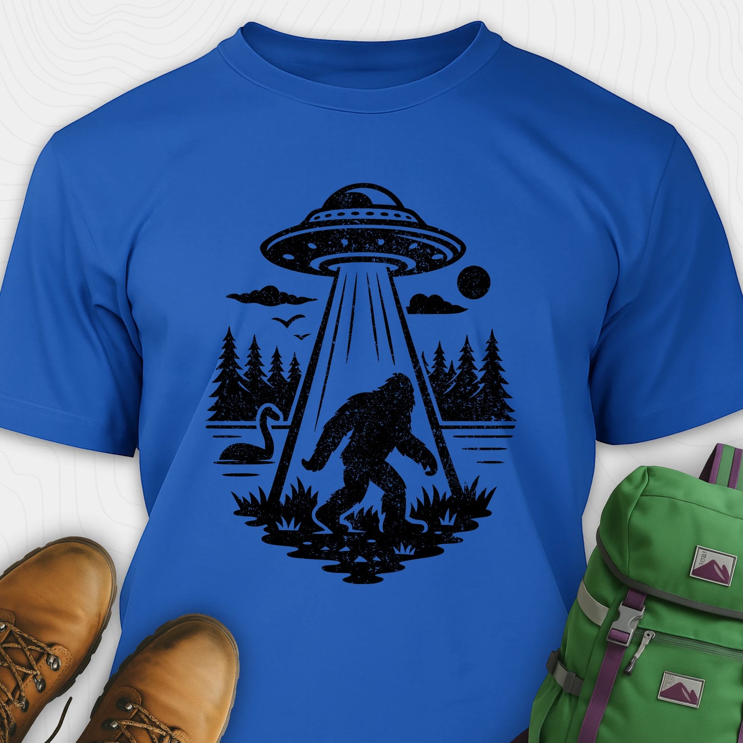 Blue monster shirt with bigfoot, forest scene, and ufo beam graphic
