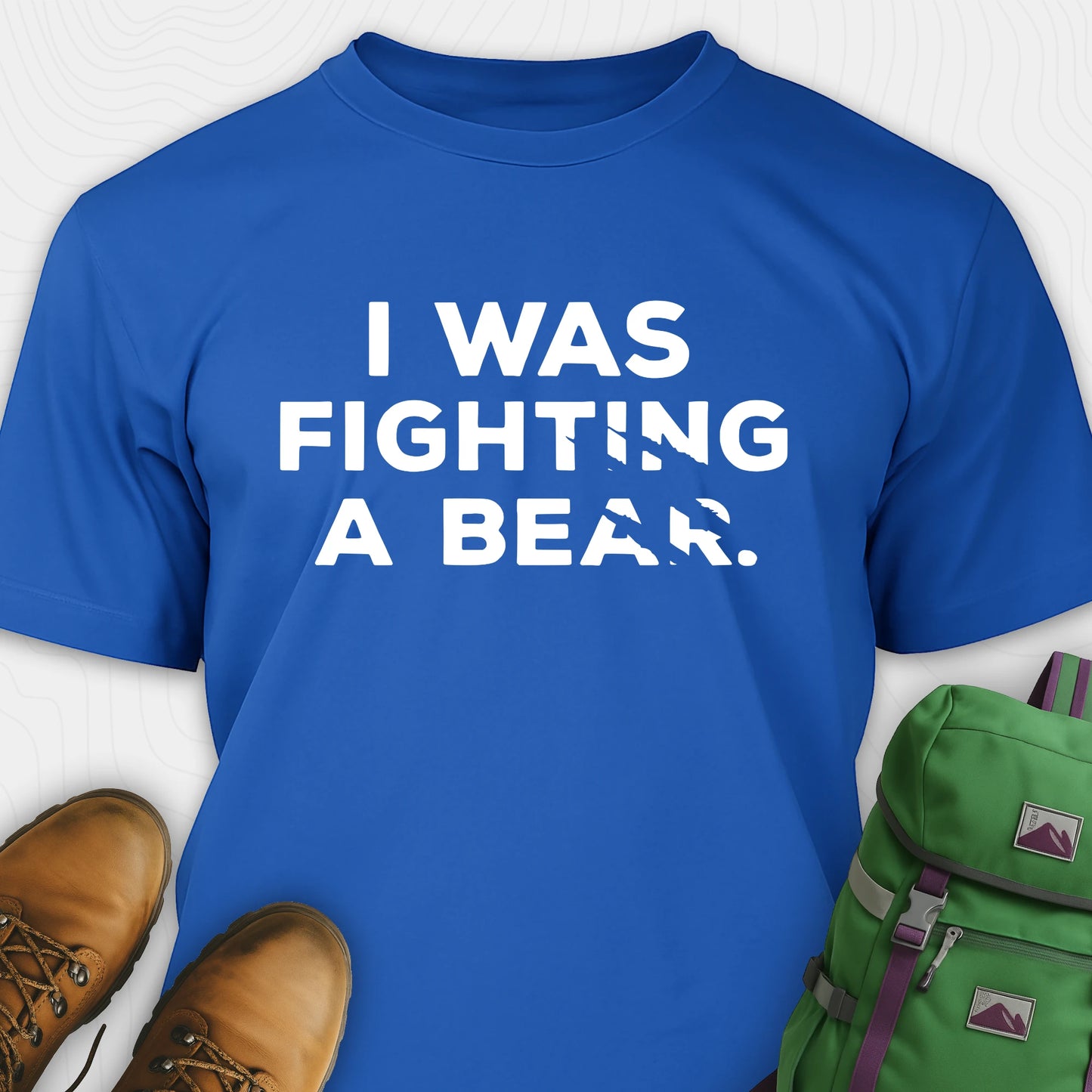 Blue I was fighting a bear shirt with a bear scratch mark graphic, paired with brown boots and a green backpack on a white background.