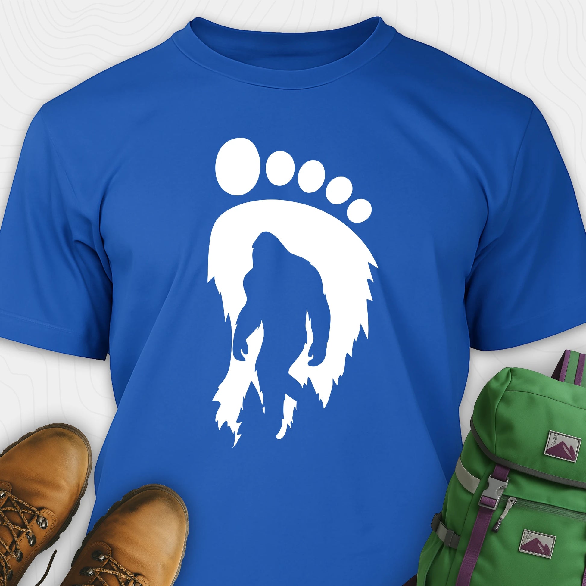 Blue bigfoot t-shirt with cryptid themed footprint graphic and sasquatch silhouette