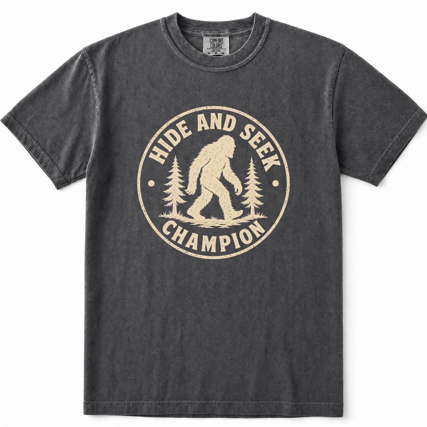 Pepper mineral-wash t-shirt with a distressed beige graphic on the front that reads 'HIDE AND SEEK CHAMPION' around an illustration of a Bigfoot figure and pine trees.