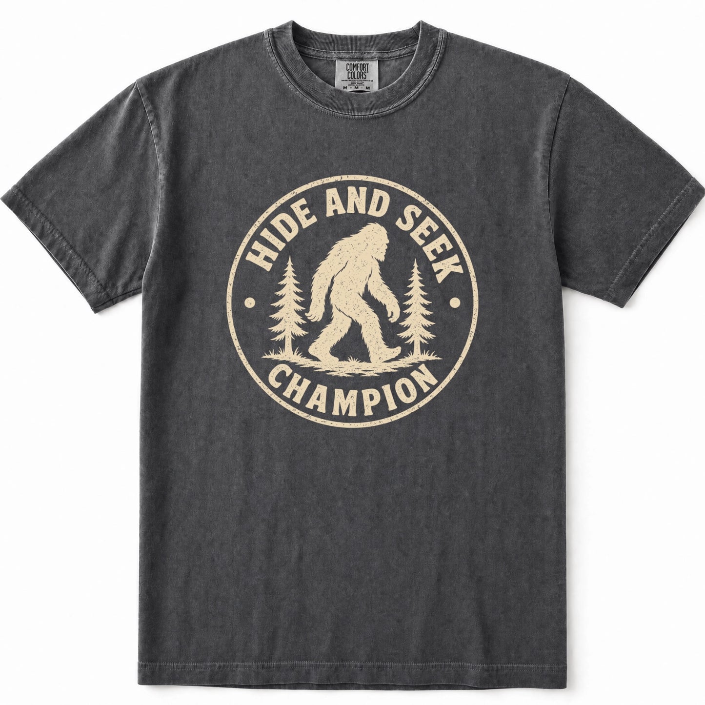 Pepper mineral-wash t-shirt with a distressed beige graphic on the front that reads 'HIDE AND SEEK CHAMPION' around an illustration of a Bigfoot figure and pine trees.