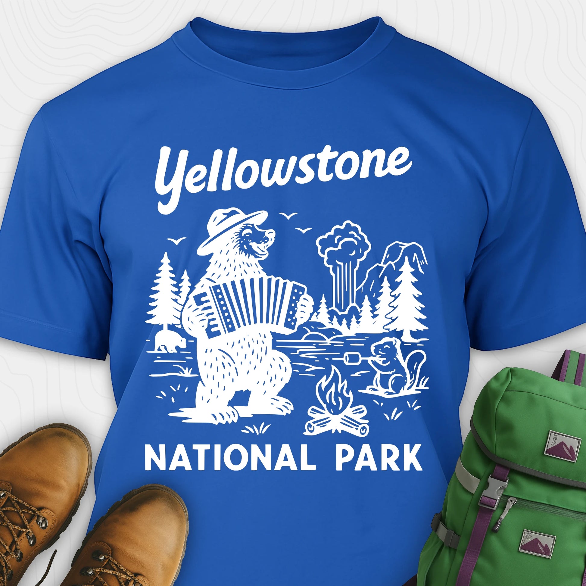 Royal blue t-shirt with a brown bear playing an accordion and “Yellowstone National Park” text, styled with hiking boots and a green backpack.