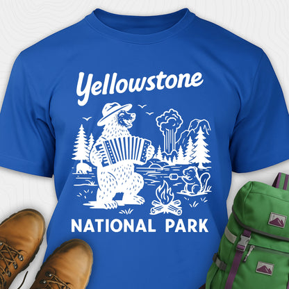 Royal blue t-shirt with a brown bear playing an accordion and “Yellowstone National Park” text, styled with hiking boots and a green backpack.