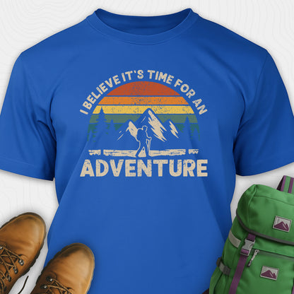 Blue backpacking shirt with mountain graphic and 'I believe it's time for an adventure' text, paired with brown boots and a green backpack.