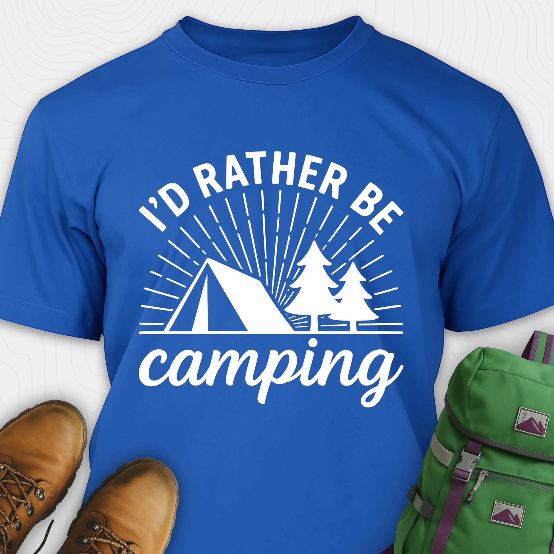 Royal blue camping shirt with 'I'd Rather Be Camping' design, brown boots, and green backpack on a white background
