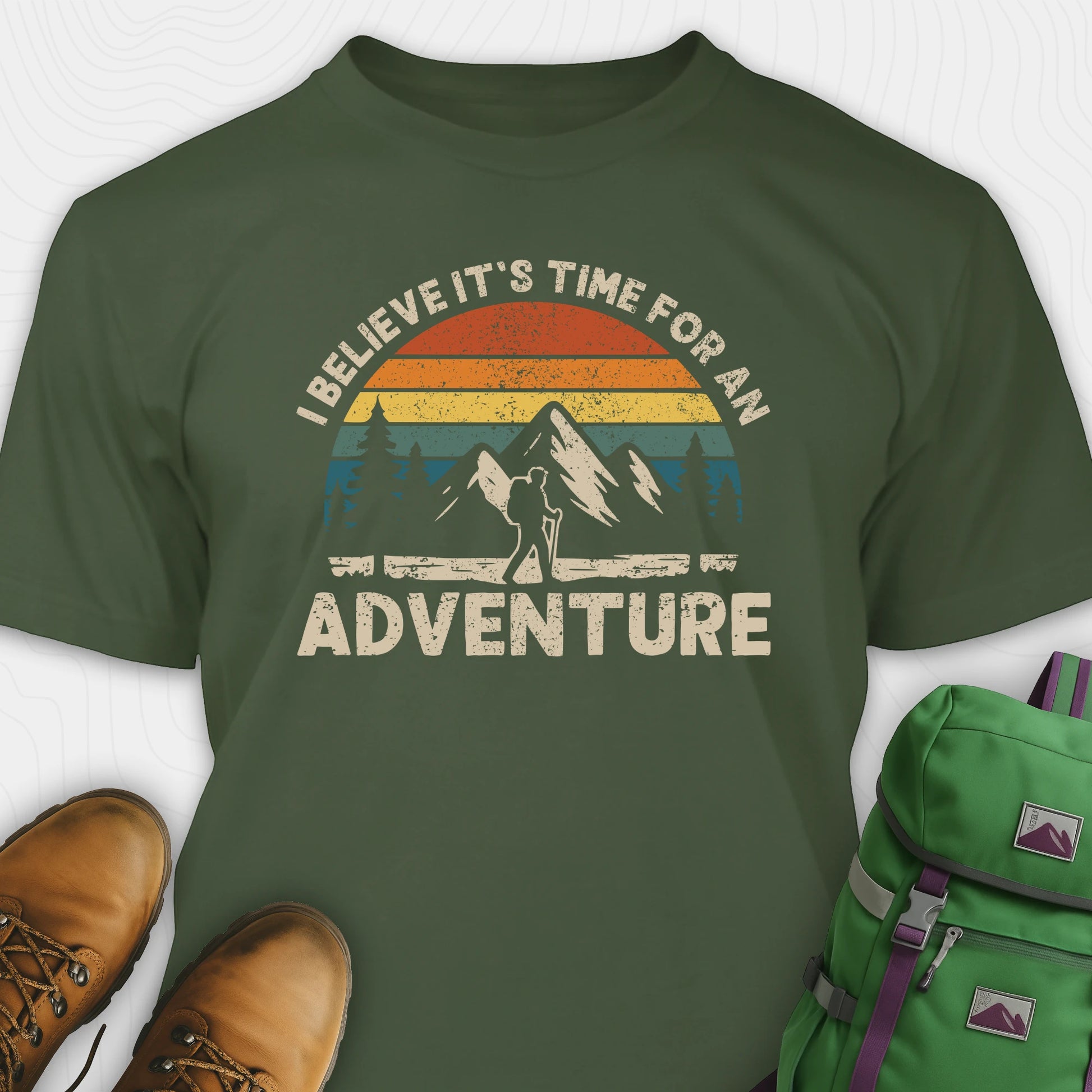 Green backpacking shirt with mountain graphic and 'I believe it's time for an adventure' text, paired with brown boots and a green backpack.