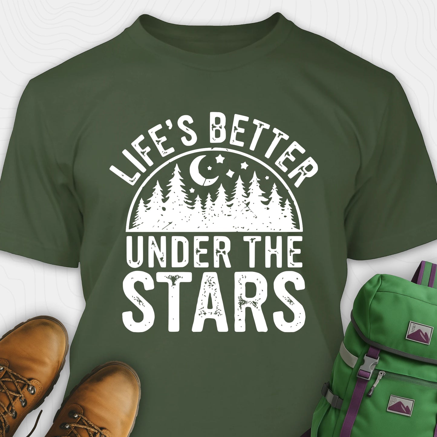 Military green Life's Better Under the Stars t-shirt with forest and moon graphic, paired with brown boots and a green backpack on a white background.