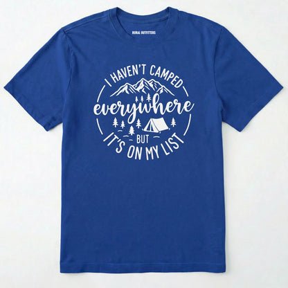 Royal funny camping shirt saying with mountains, trees, tent graphic and "I Haven't Camped Everywhere But It's On My List" text on a white background.