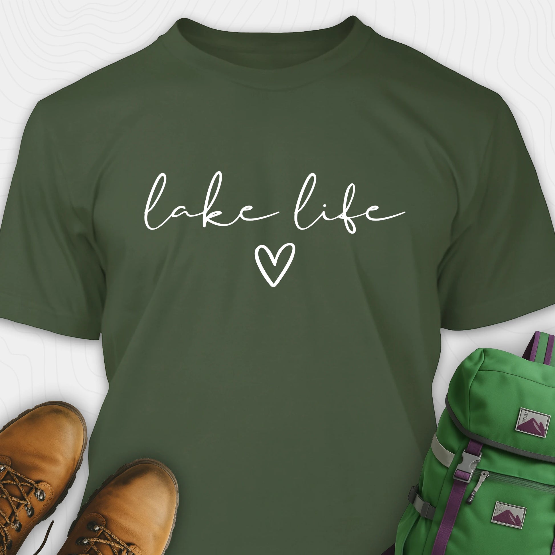 Military green lake life shirt with 'lake life' text and heart symbol, paired with brown boots and a green backpack on a white background.