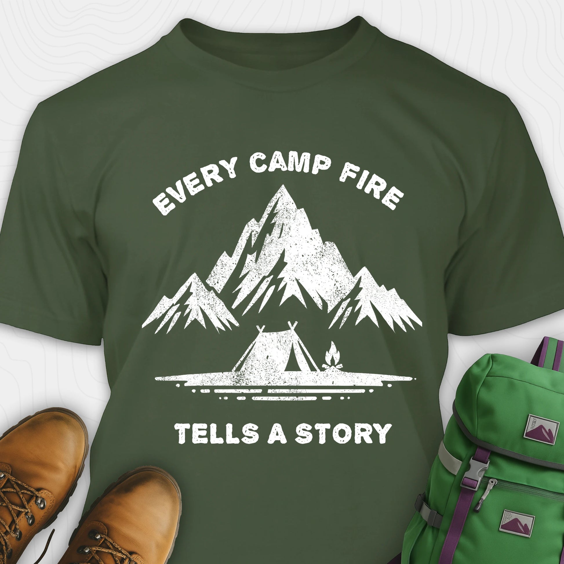 Green campfire story shirt with mountains and tent graphic and "every camp fire tells a story" text