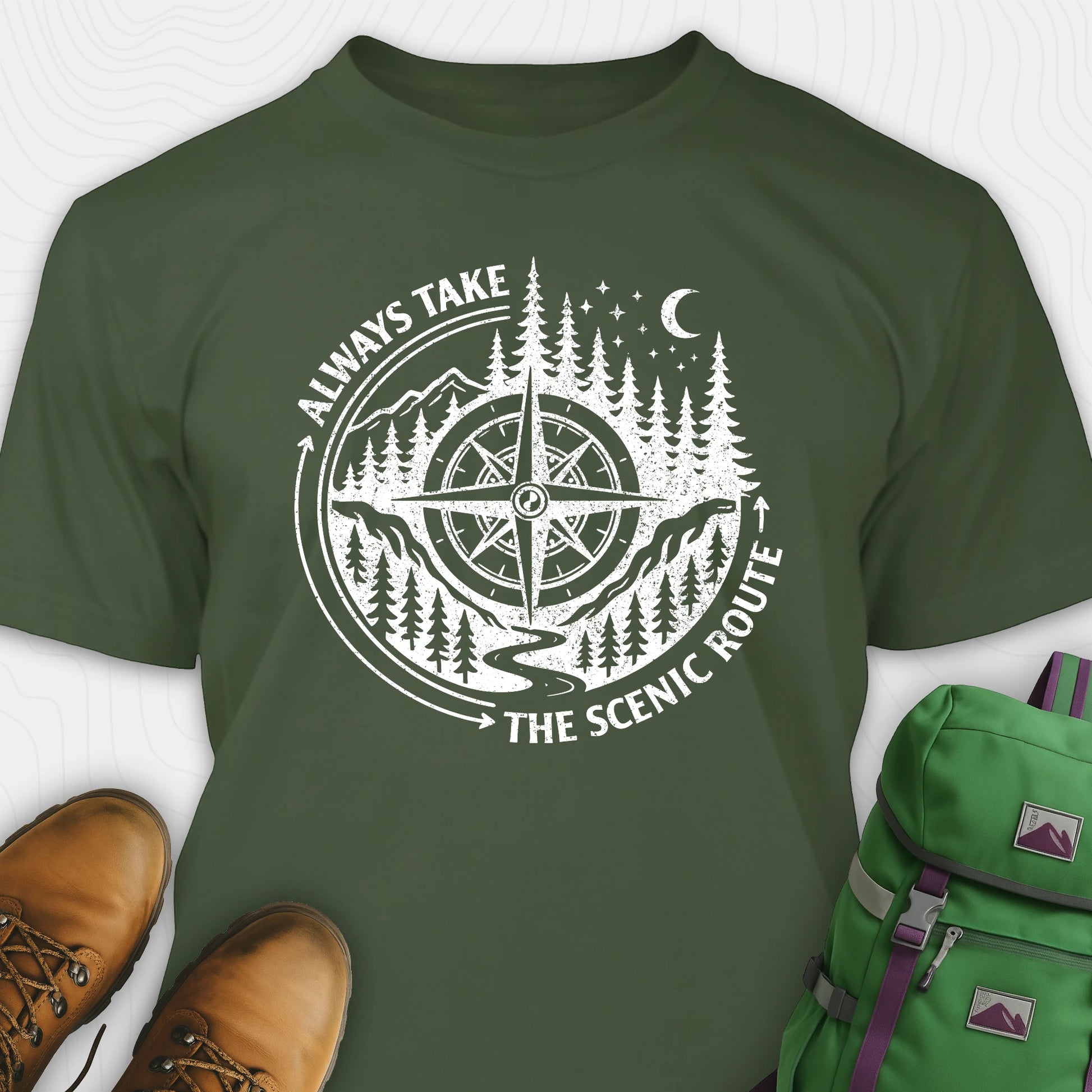 Green always take the scenic route t-shirt with compass graphic and text, paired with hiking boots and a green backpack.
