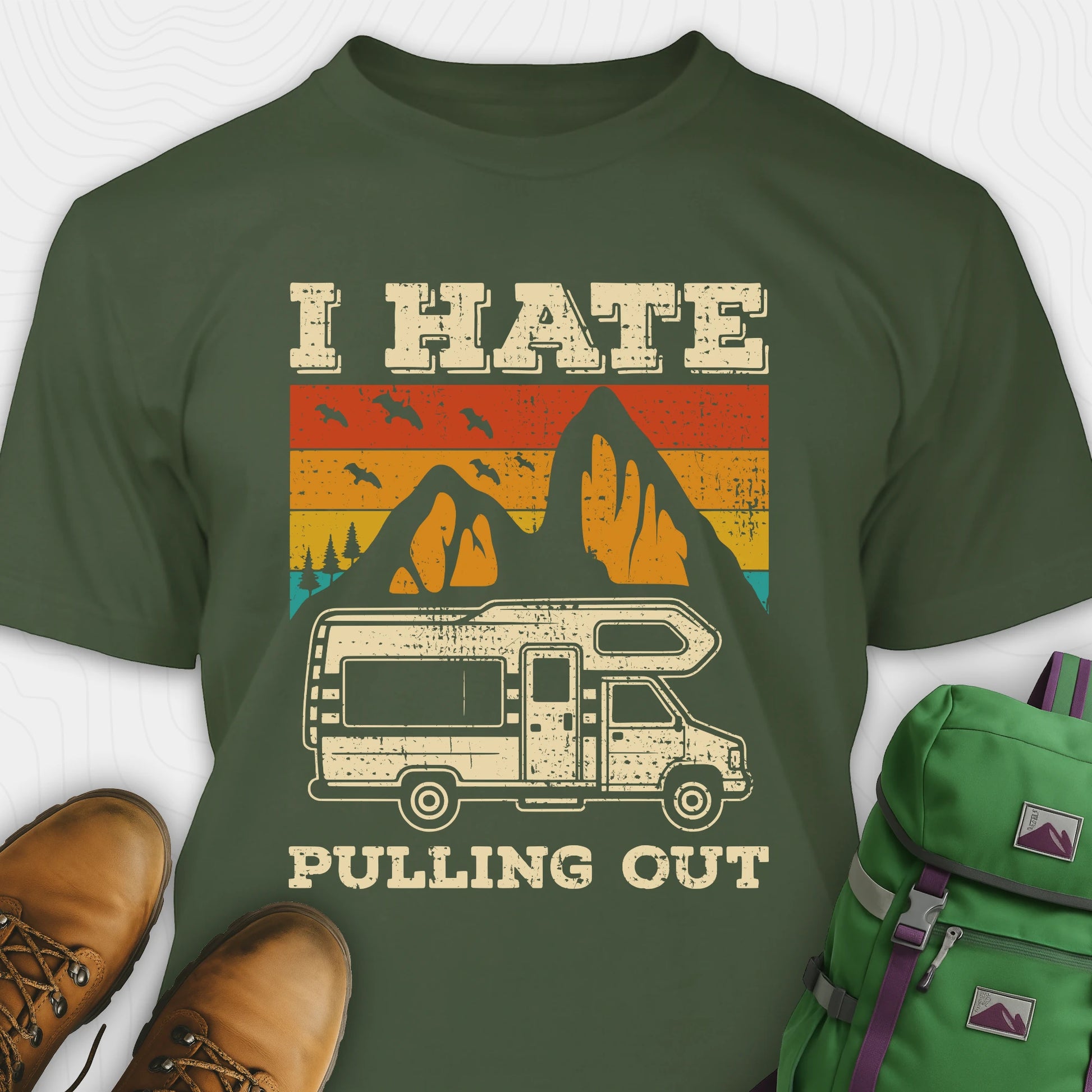 Green I hate pulling out shirt with a graphic design of an RV and mountains, displayed with brown boots and a green backpack.