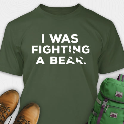 Green I was fighting a bear shirt with a bear scratch mark graphic, paired with brown boots and a green backpack on a white background.