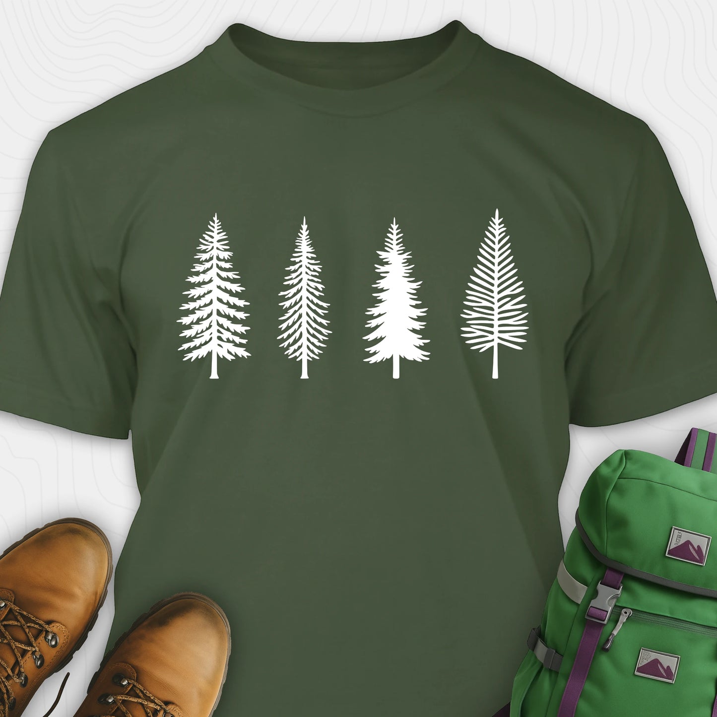 Military green pine tree shirt with white minimalist forest graphic, brown boots, and a green backpack on a light gray background
