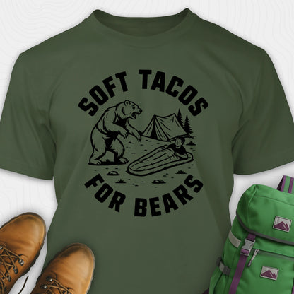 Green funny bear shirt with bear graphic and text 'Soft Tacos for Bears' on a white background. surrounded by hiking boots and a green backpack.