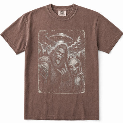 Espresso brown short-sleeve crewneck t-shirt featuring a distressed graphic print of Bigfoot and an alien making peace signs, set against a plain white background.