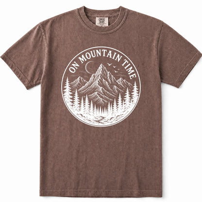 Espresso short-sleeve crewneck t-shirt with a white circular graphic on the chest depicting mountains, pine trees, and a crescent moon, with the text 'ON MOUNTAIN TIME'.