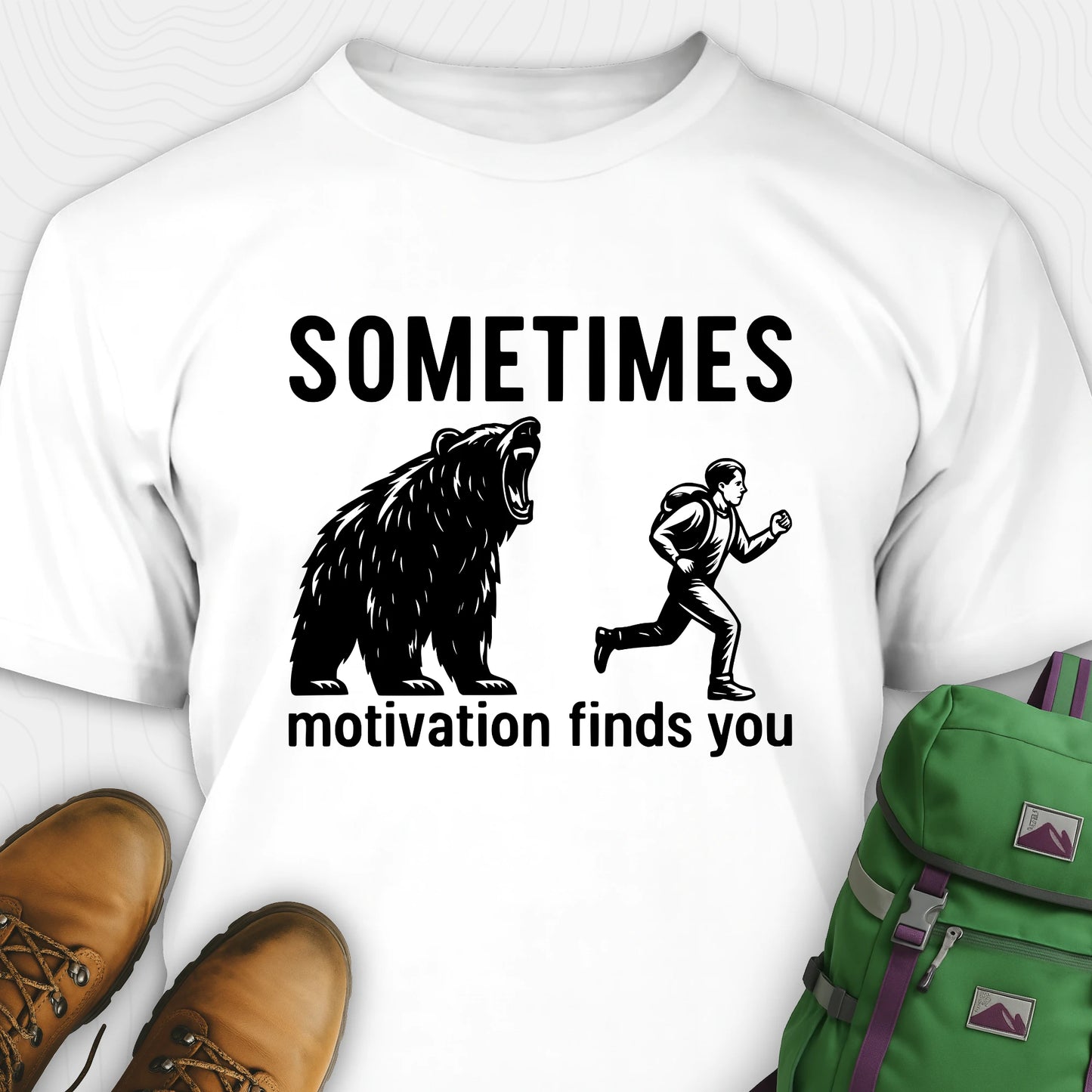 White motivational t-shirt with bear and person graphic and text 'SOMETIMES motivation finds you' on a white background.