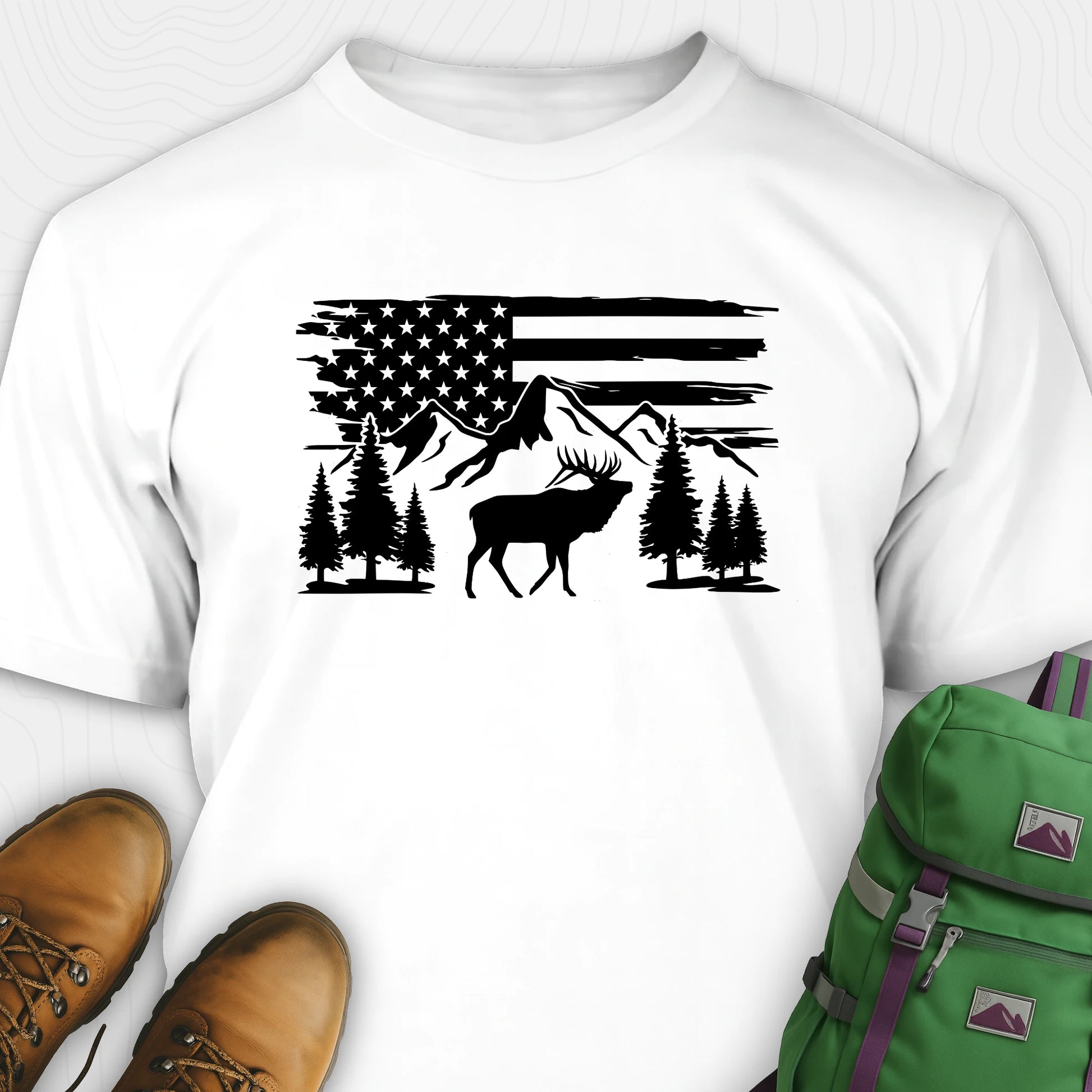 White deer t-shirt with black graphic design of an American flag, trees, and a moose, accompanied by brown boots and a green backpack.