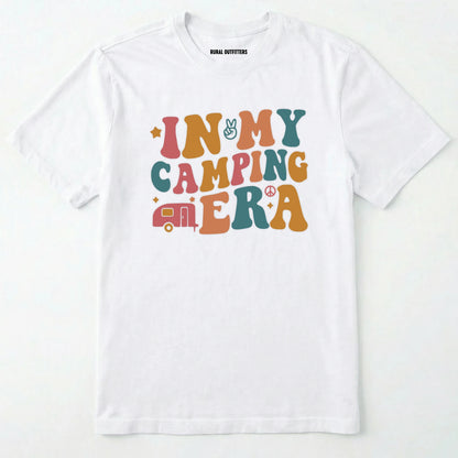 White cute camping shirt with colorful retro ⊜in my camping era⊝ graphic on a white background.