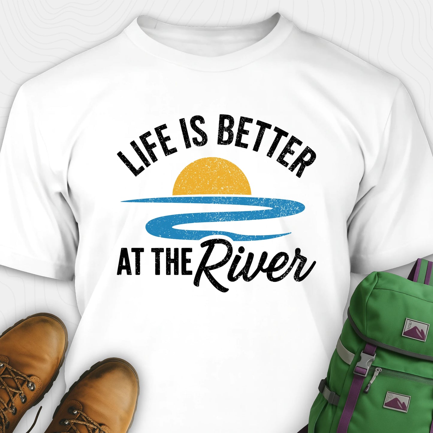 White river shirt with 'Life is Better at the River' design, paired with brown boots and a green backpack on a light gray background.