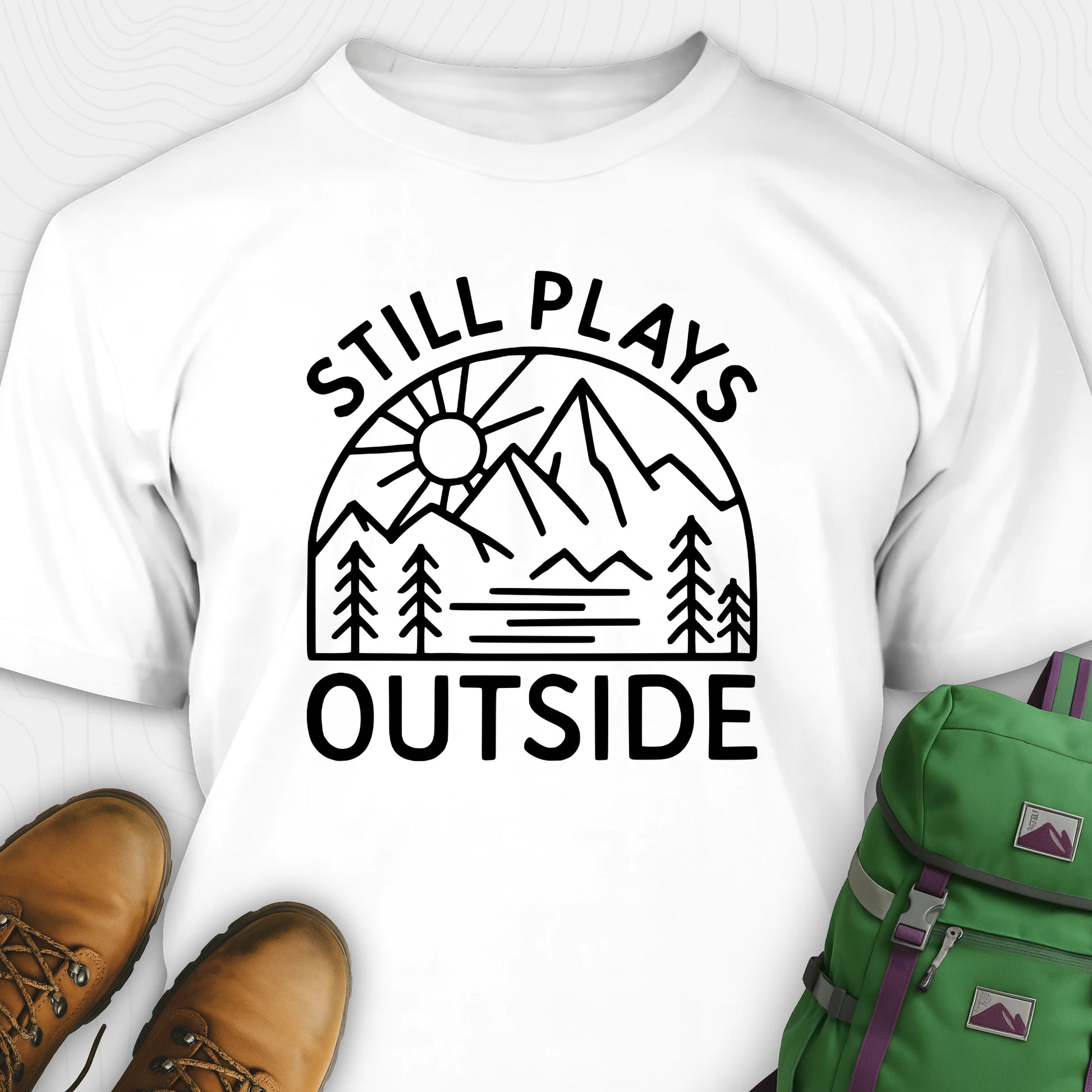 White t-shirt with 'Still Plays Outside' graphic design, paired with brown boots and a green backpack on a light gray background.