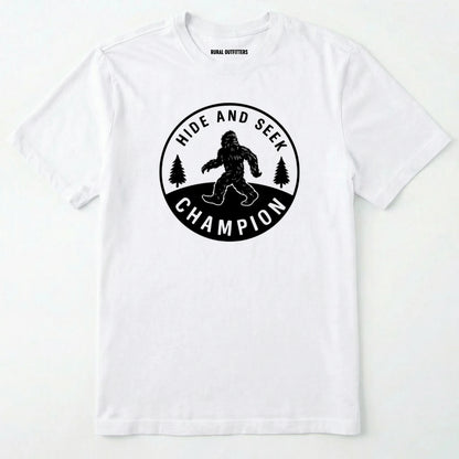 White bigfoot hide and seek champion shirt with forest emblem on a white background.