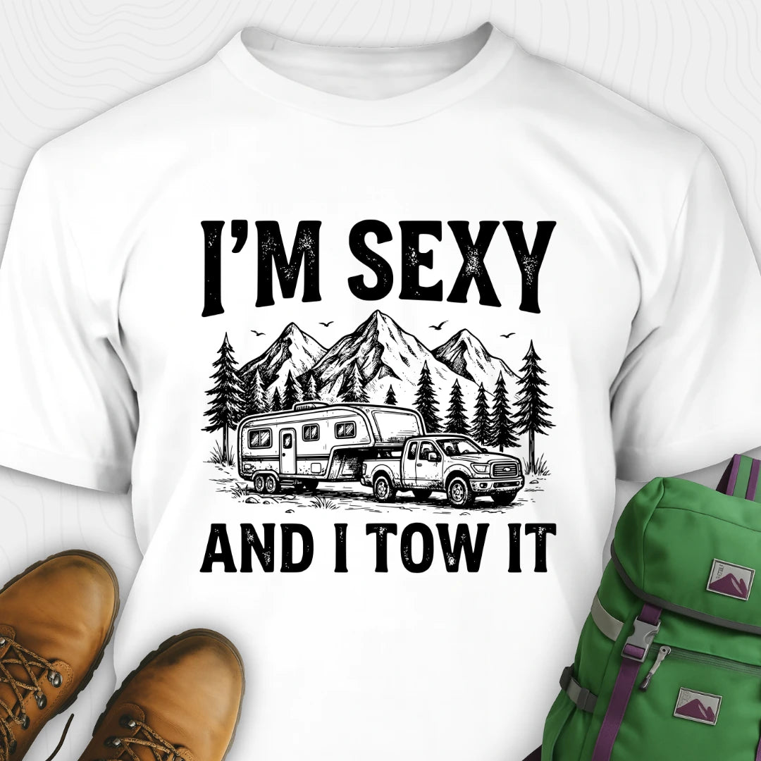 White t-shirt with 'I'm Sexy and I Tow It' graphic design featuring a truck and camper, paired with brown shoes and a green backpack.