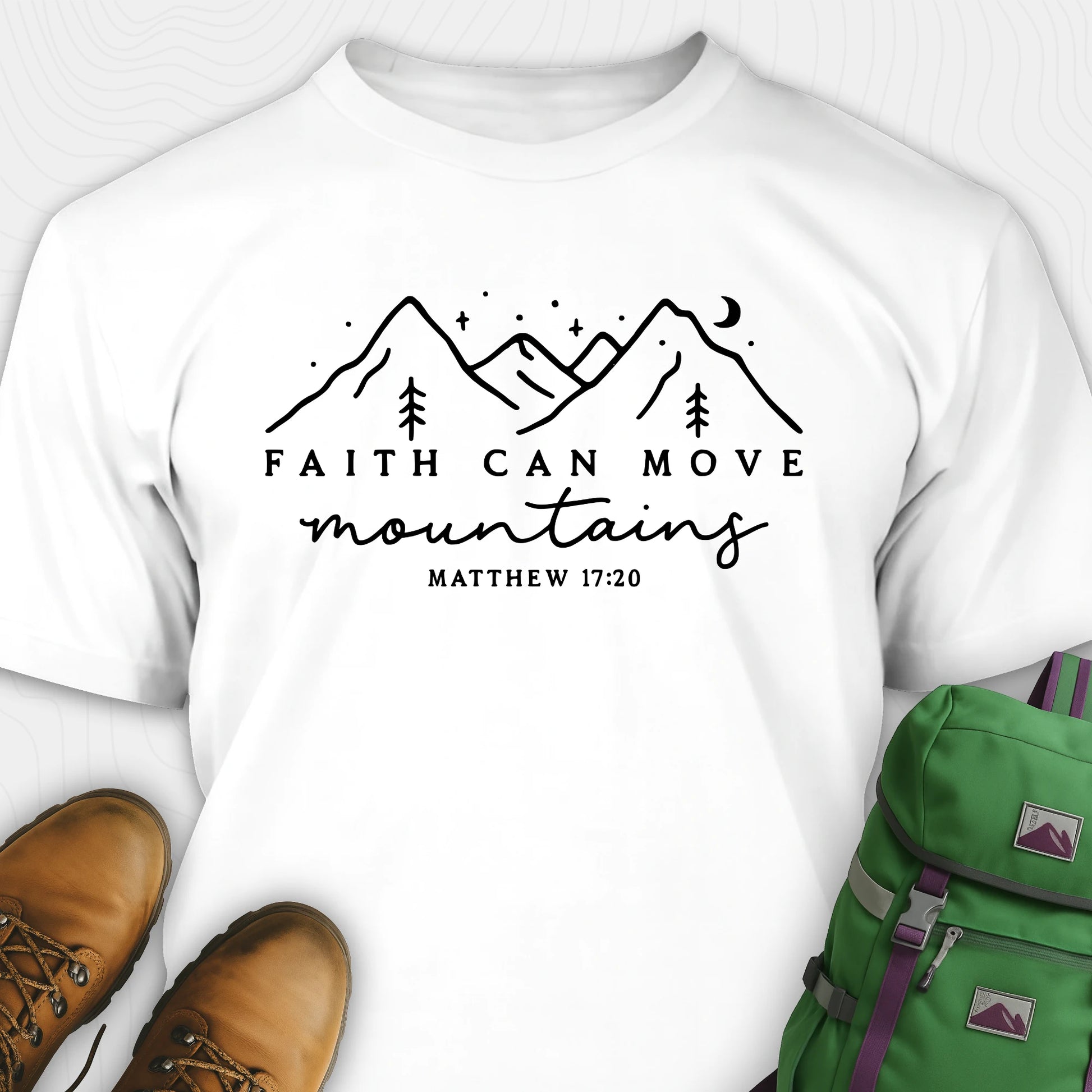 White faith can move mountains shirt with mountain scripture design, paired with hiking boots and a green backpack.