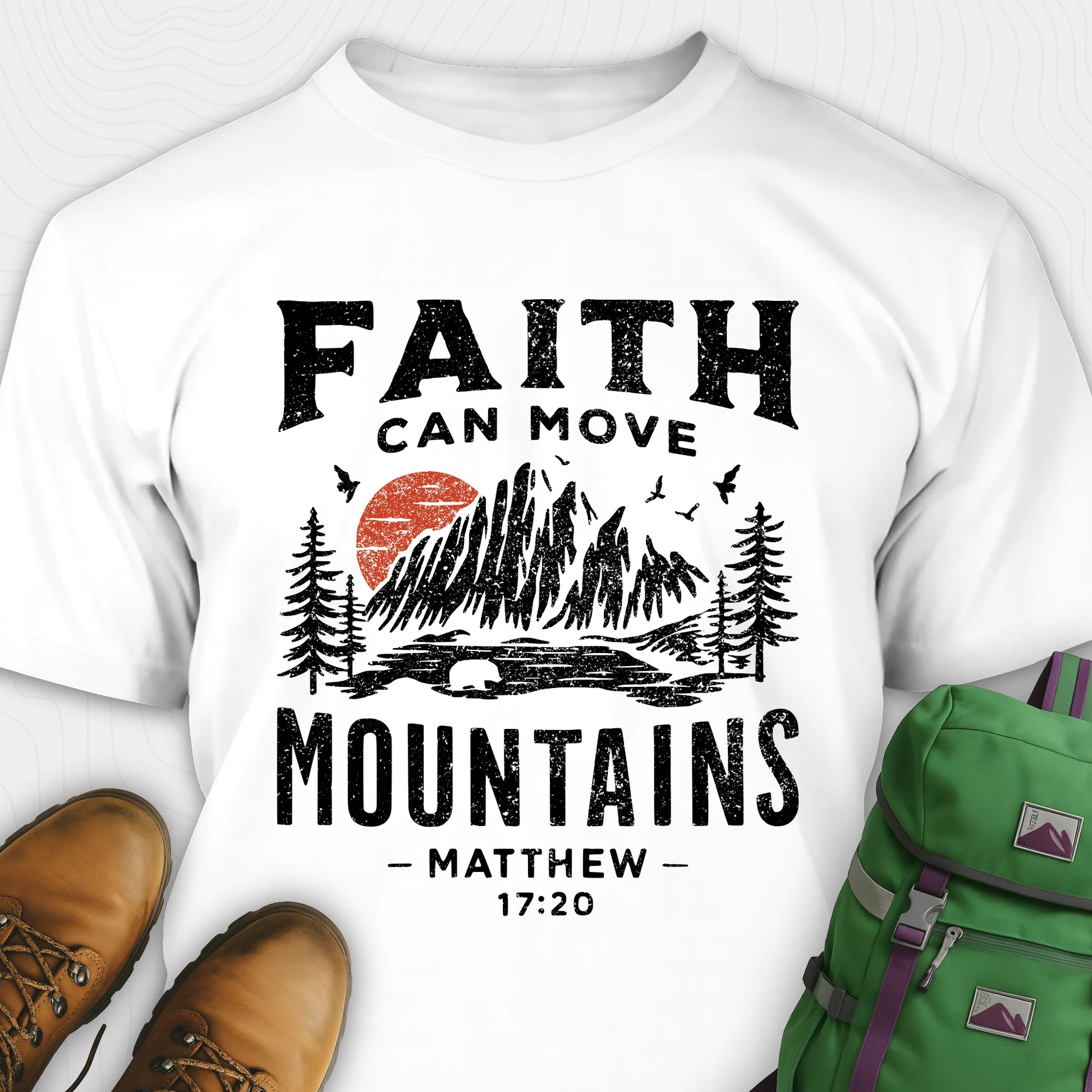 White bible verse t-shirt with 'Faith can move mountains' design and hiking boots and backpack on a white background