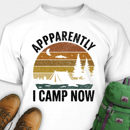 White t-shirt with “Apparently I Camp Now” in white text and a vintage sunset camping scene with tent, trees, and moon.