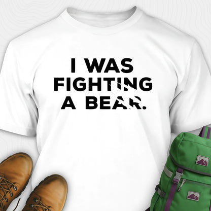 White I was fighting a bear shirt with a bear scratch mark graphic, paired with brown boots and a green backpack on a white background.