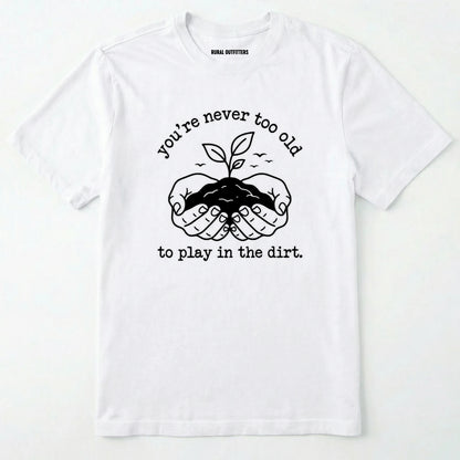 White t-shirt with black graphic and text 'you're never too old to play in the dirt' on a white background