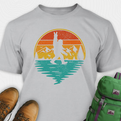 Sport grey bigfoot shirt for men with retro mountain graphic beside boots and green backpack