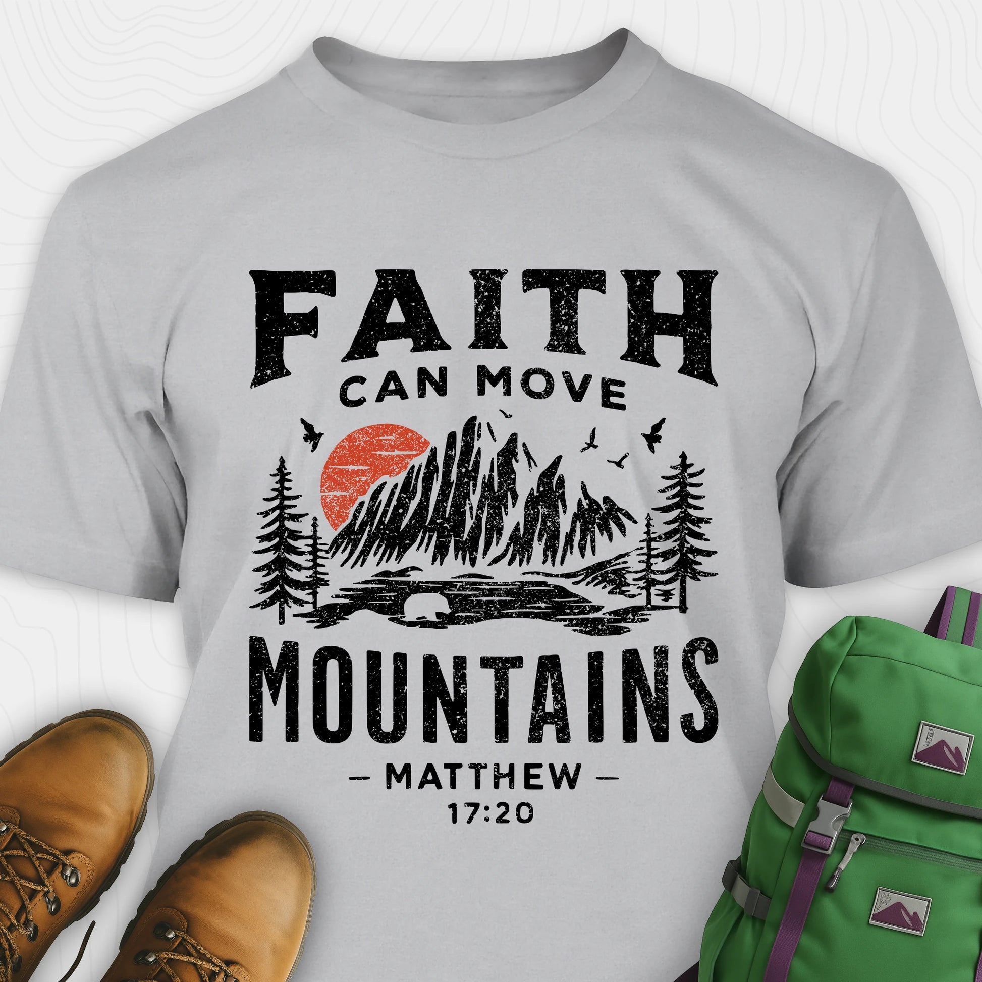 Grey bible verse t-shirt with 'Faith can move mountains' design and hiking boots and backpack on a white background