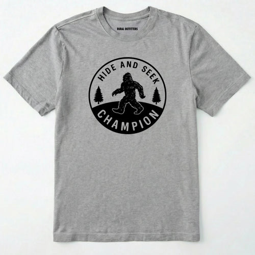 Sport Grey Bigfoot hide and seek champion shirt with forest emblem on a white background.
