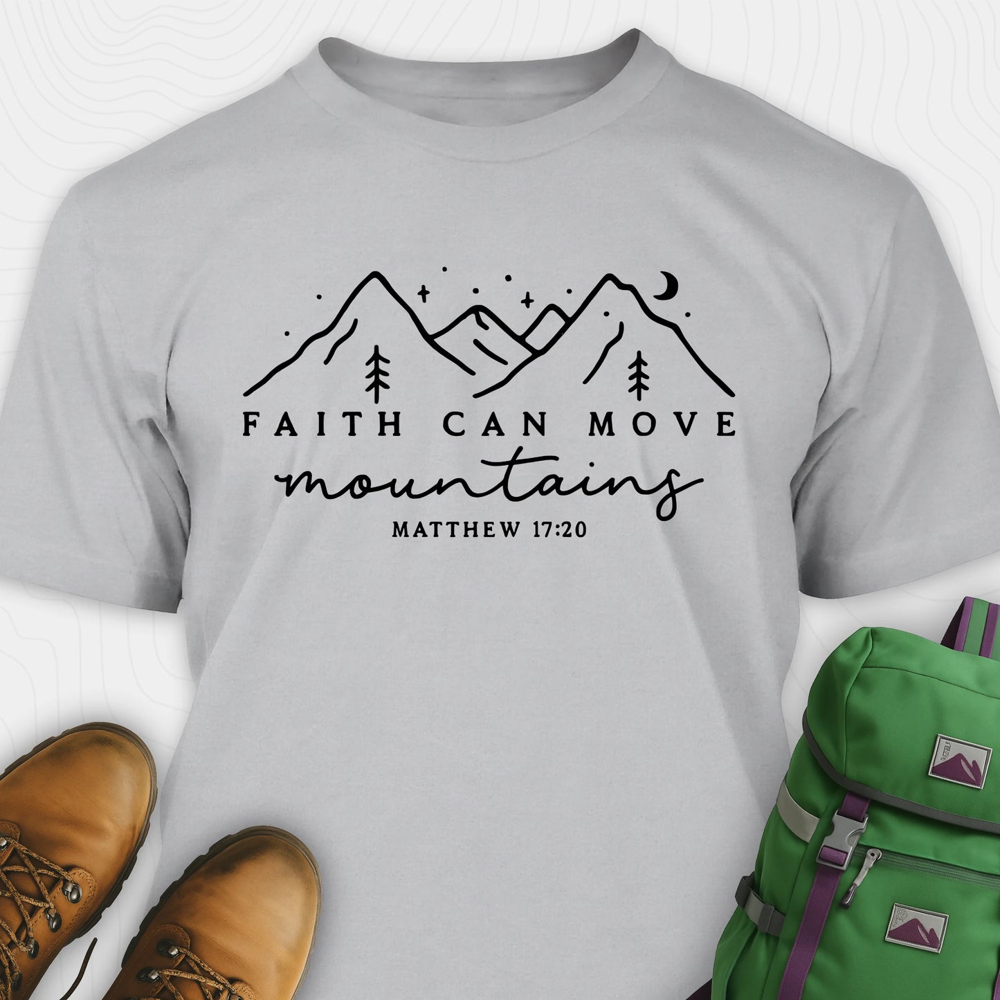 Grey faith can move mountains shirt with mountain scripture design, paired with hiking boots and a green backpack.