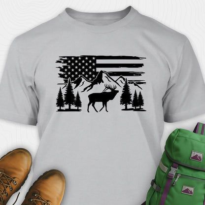 Gray deer t-shirt with black graphic design of an American flag, trees, and a moose, accompanied by brown boots and a green backpack.