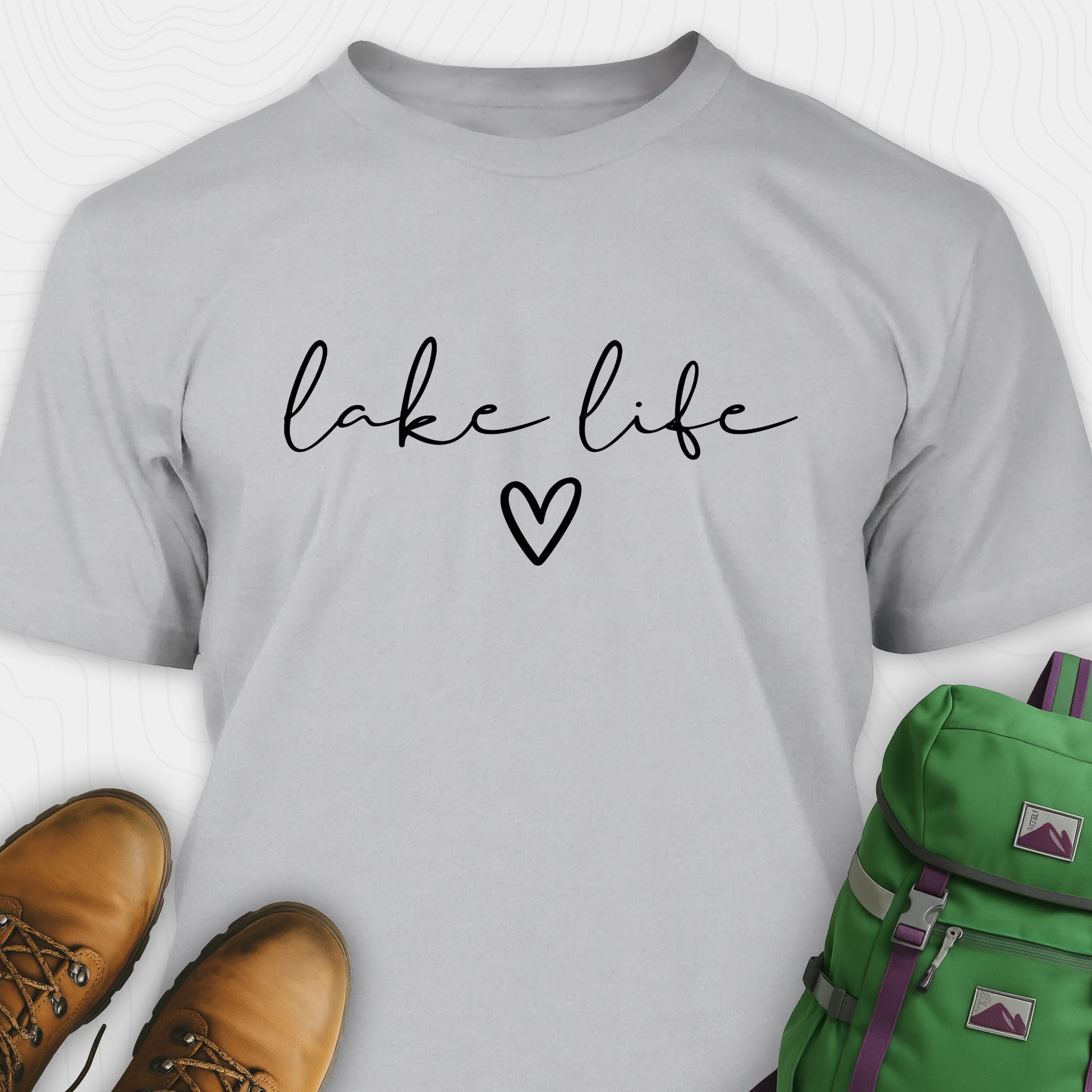 Sport grey lake life shirt with 'lake life' text and heart, paired with brown boots and a green backpack on a white background.
