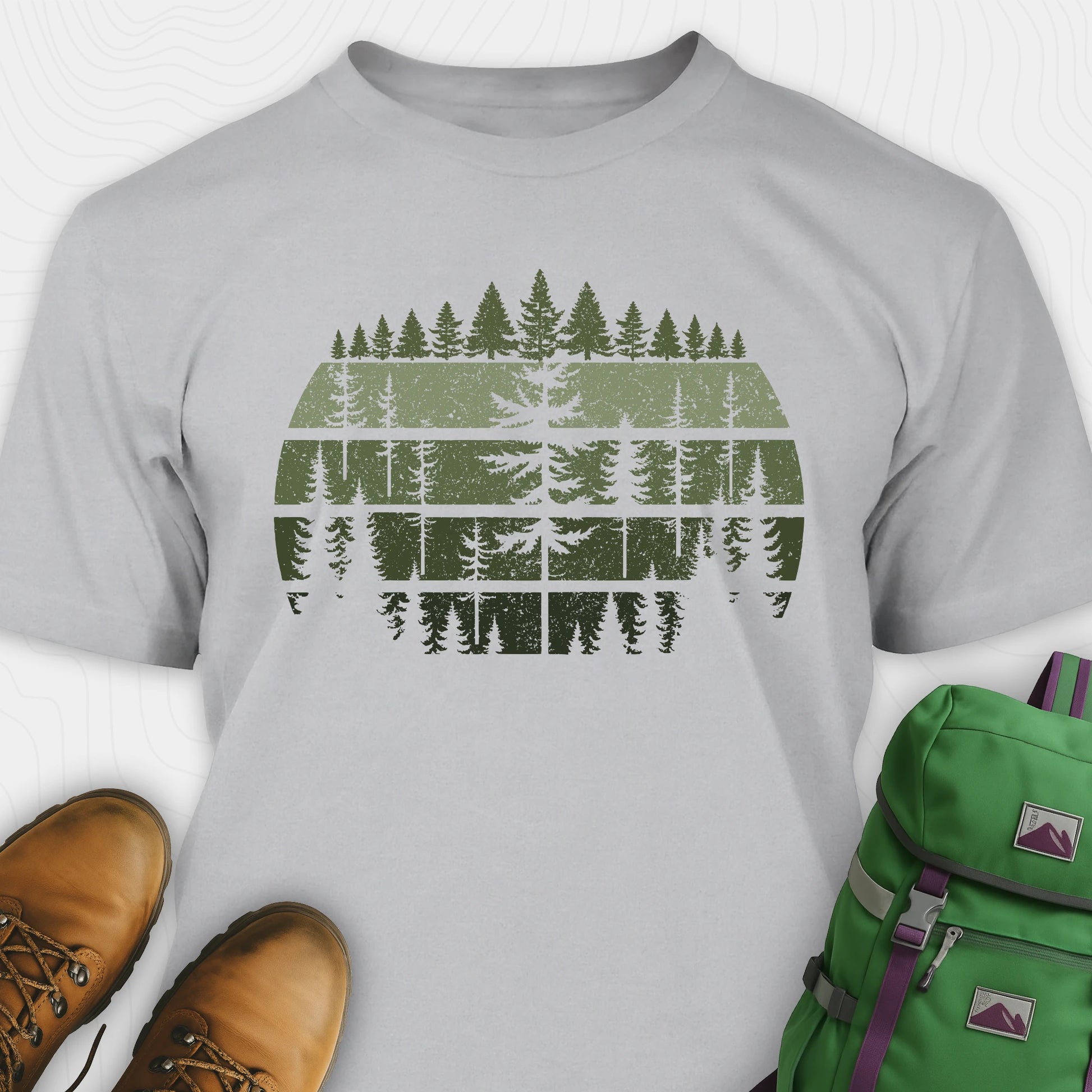 Grey forest shirt with distressed pine tree design, and green backpack on a white background