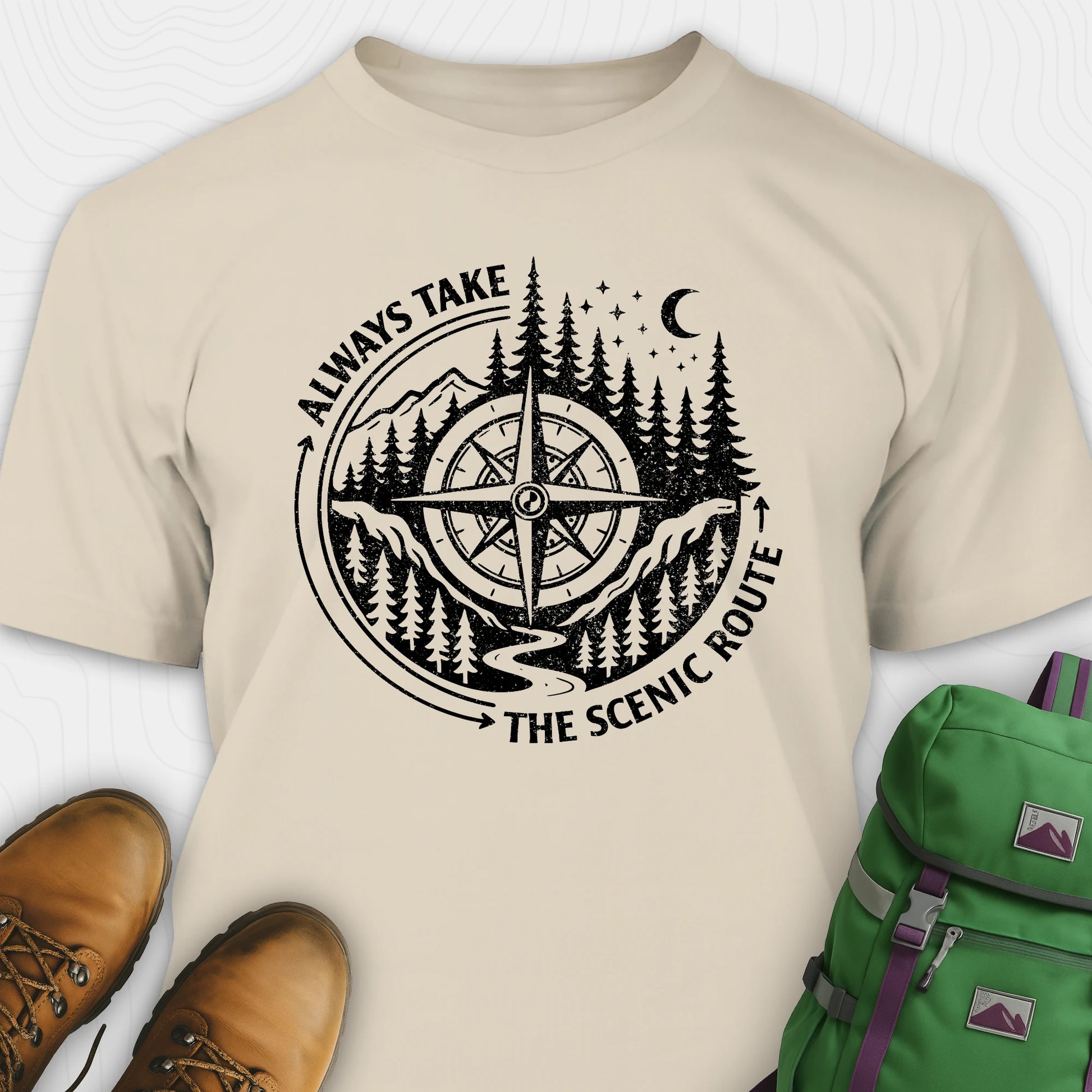 Natural always take the scenic route t-shirt with compass graphic and text, paired with hiking boots and a green backpack.