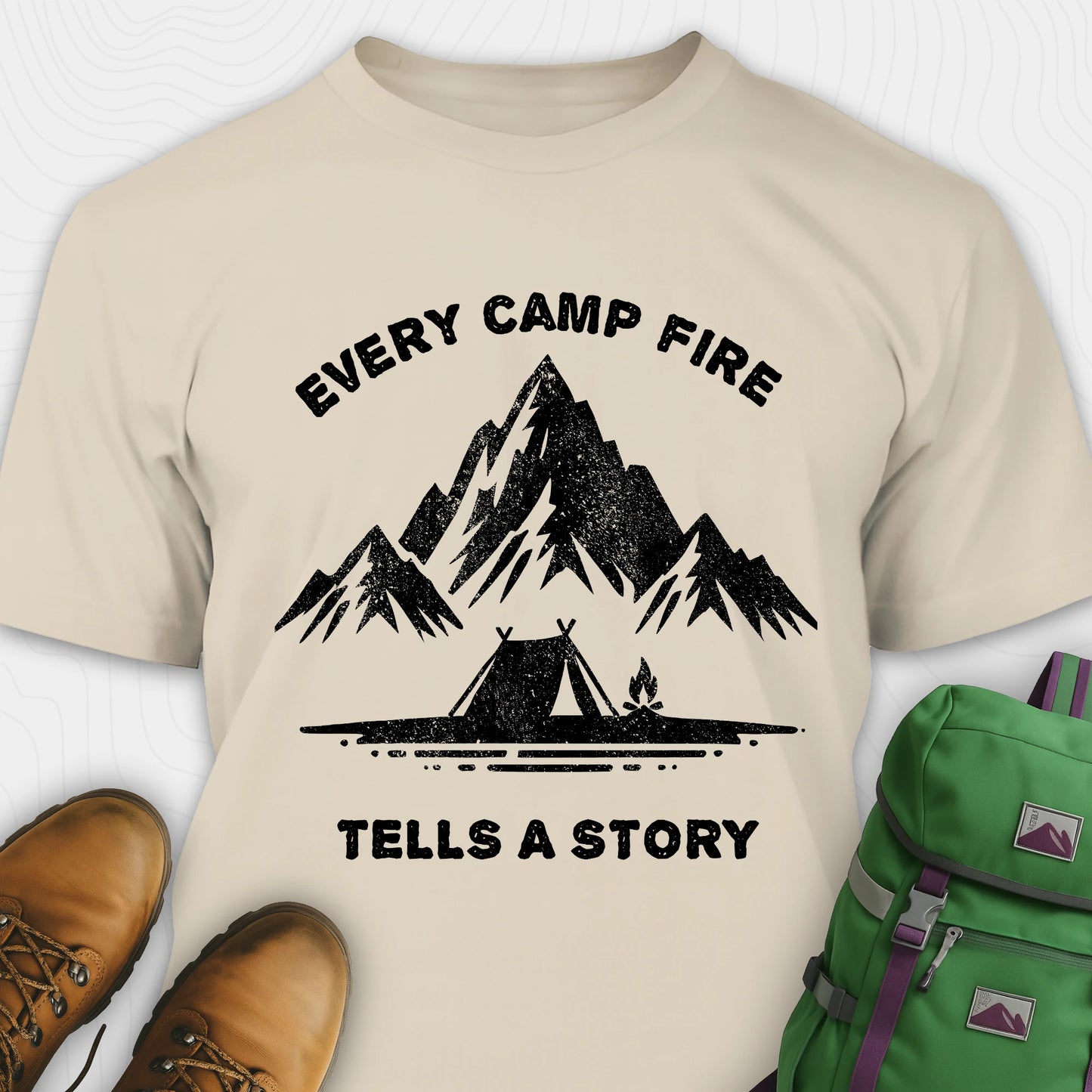 Sand campfire story shirt with mountains and tent graphic and "every camp fire tells a story" text