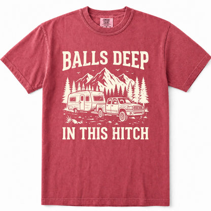 Crimson short-sleeve crewneck t-shirt in a washed, heathered red color, featuring a cream-colored graphic print of a pickup truck towing a camper trailer with mountains and pine trees in the background. The text reads 'BALLS DEEP' above the graphic and 'IN THIS HITCH' below.