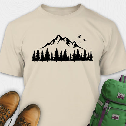 Sand wild t-shirt with a minimalist mountain and pine tree graphic, shown flat with boots and a backpack