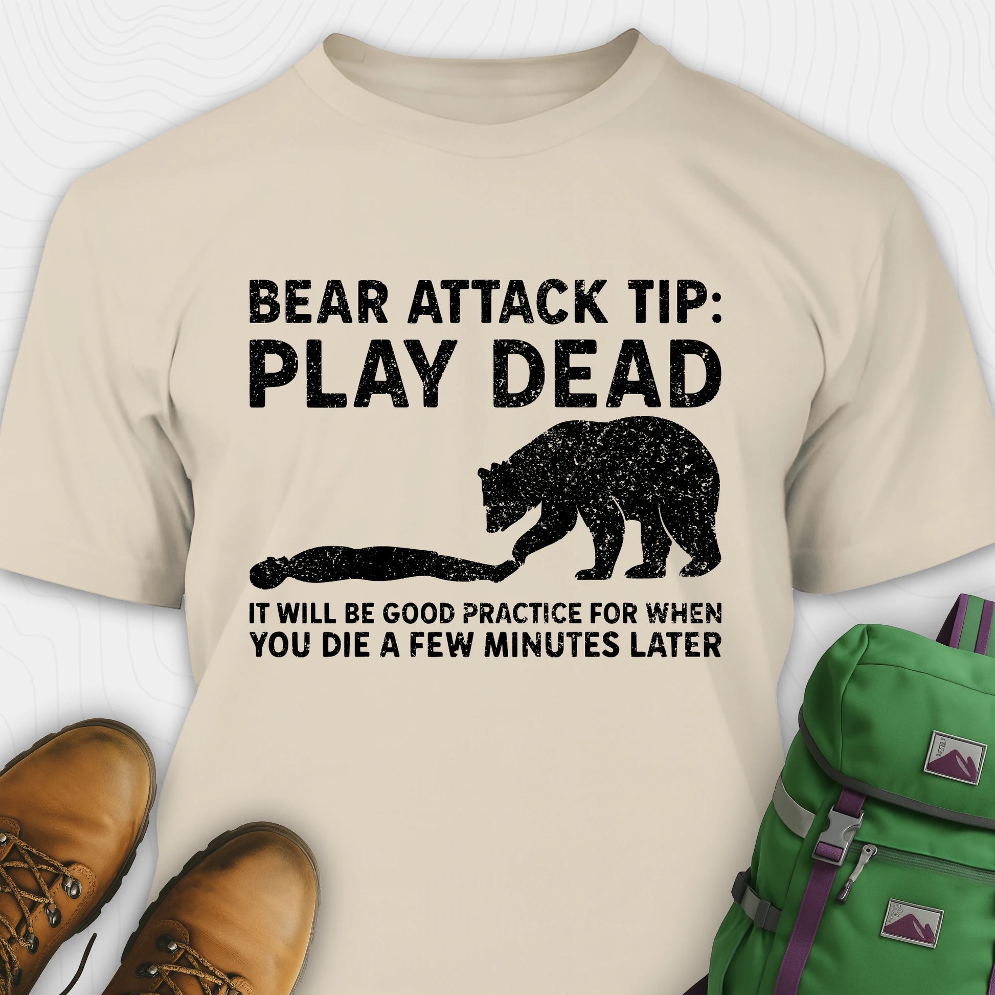 Sand bear tee shirt with bear graphic and text, paired with brown boots and a green backpack on a white background.