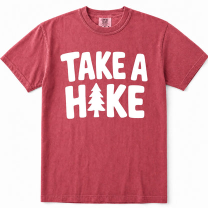 Crimson short-sleeve crewneck t-shirt in a washed, heathered red color, featuring the phrase 'TAKE A HIKE' printed in bold white capital letters across the chest, with a pine tree icon replacing the letter 'I'.